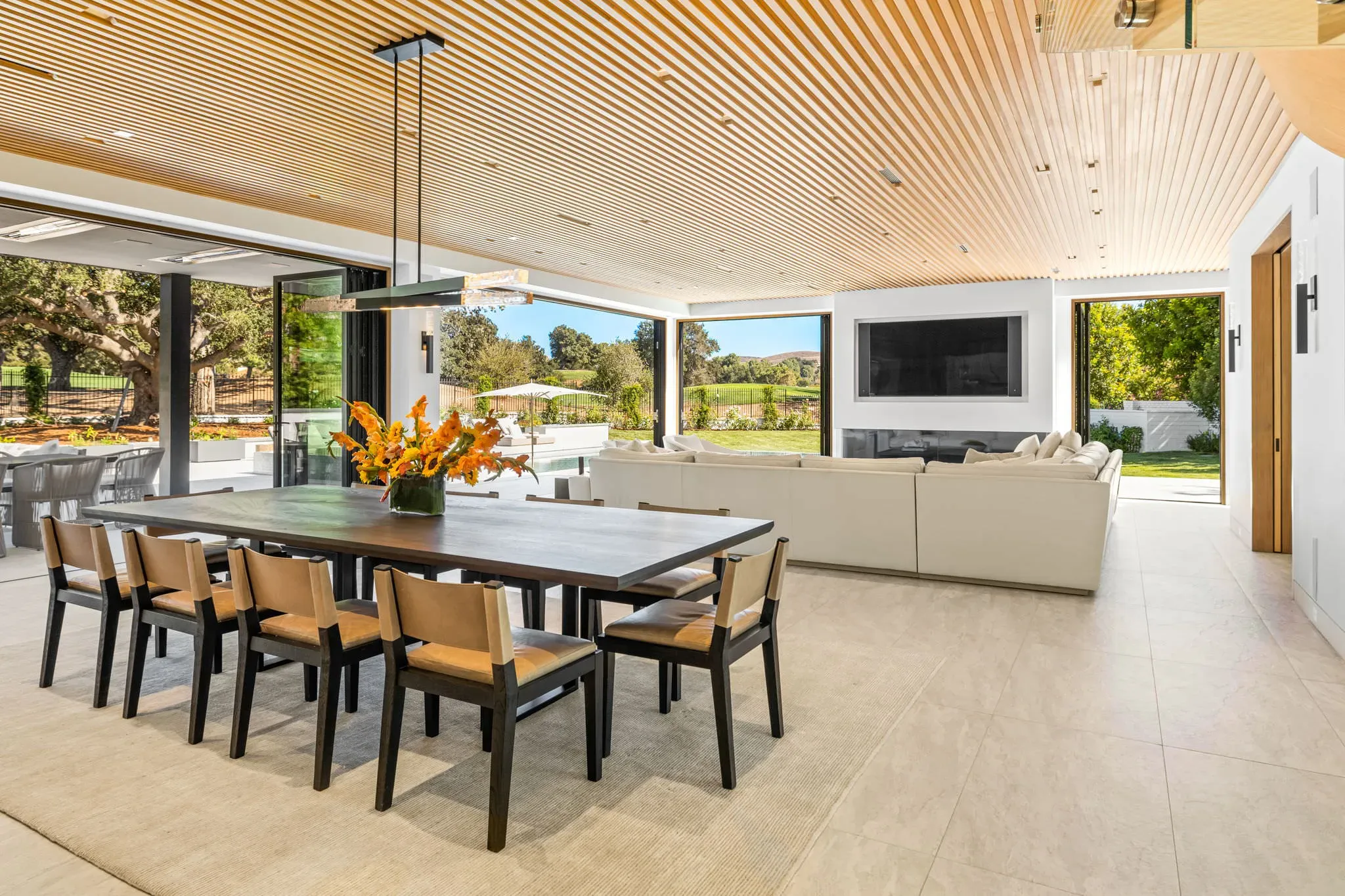 Dining area under a slatted oak ceiling with walls of glass to the yard