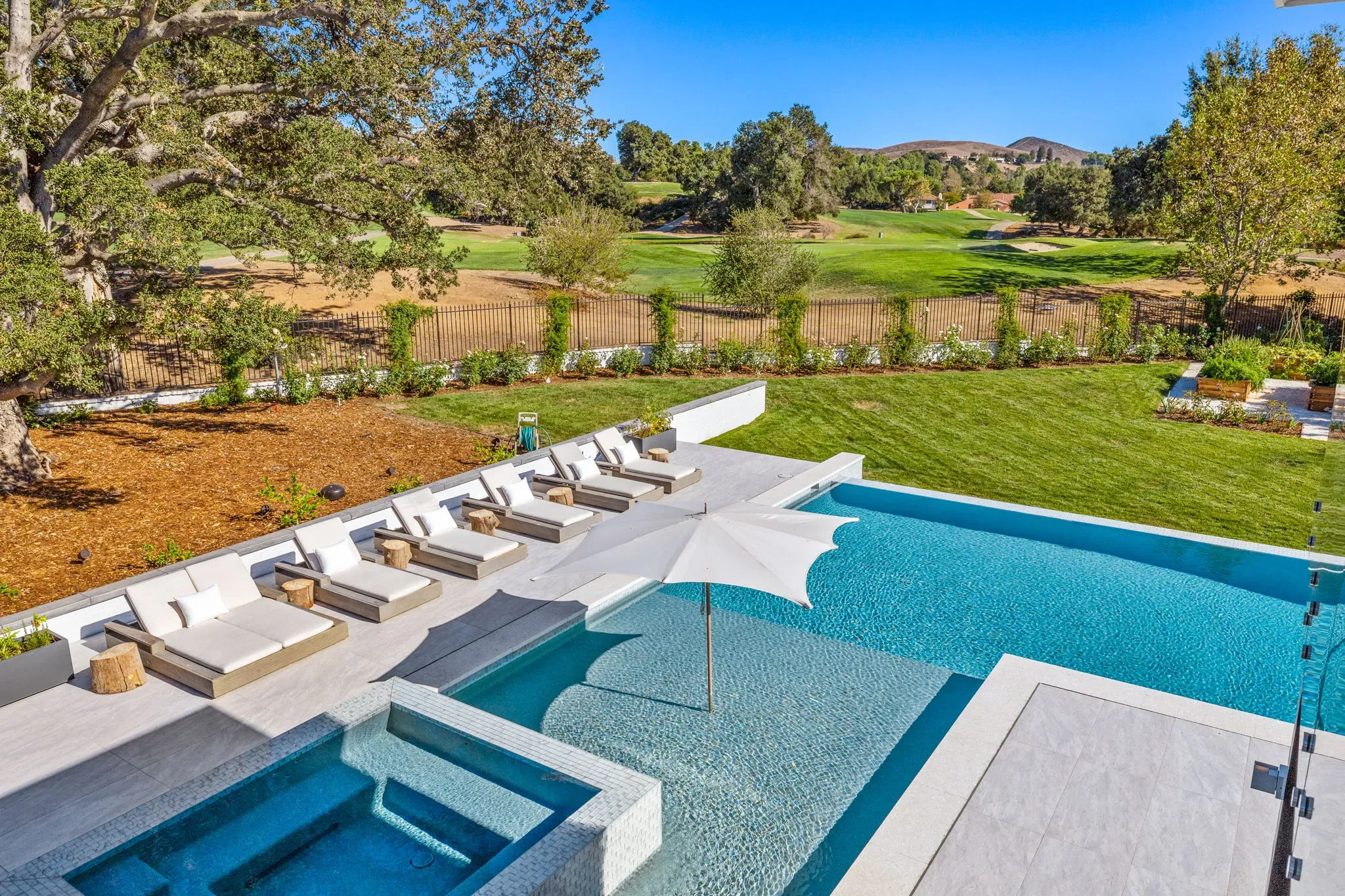 Modern pool with baja shelf, umbrellas, and cabana deck